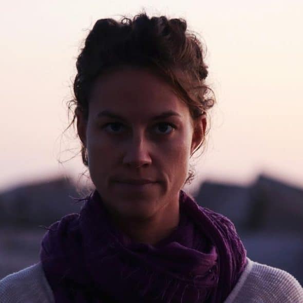 A woman standing outdoors at dusk with a calm, focused expression.