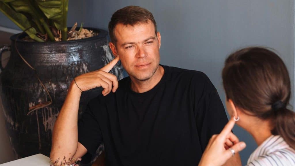 A man and woman sitting together and talking indoors.