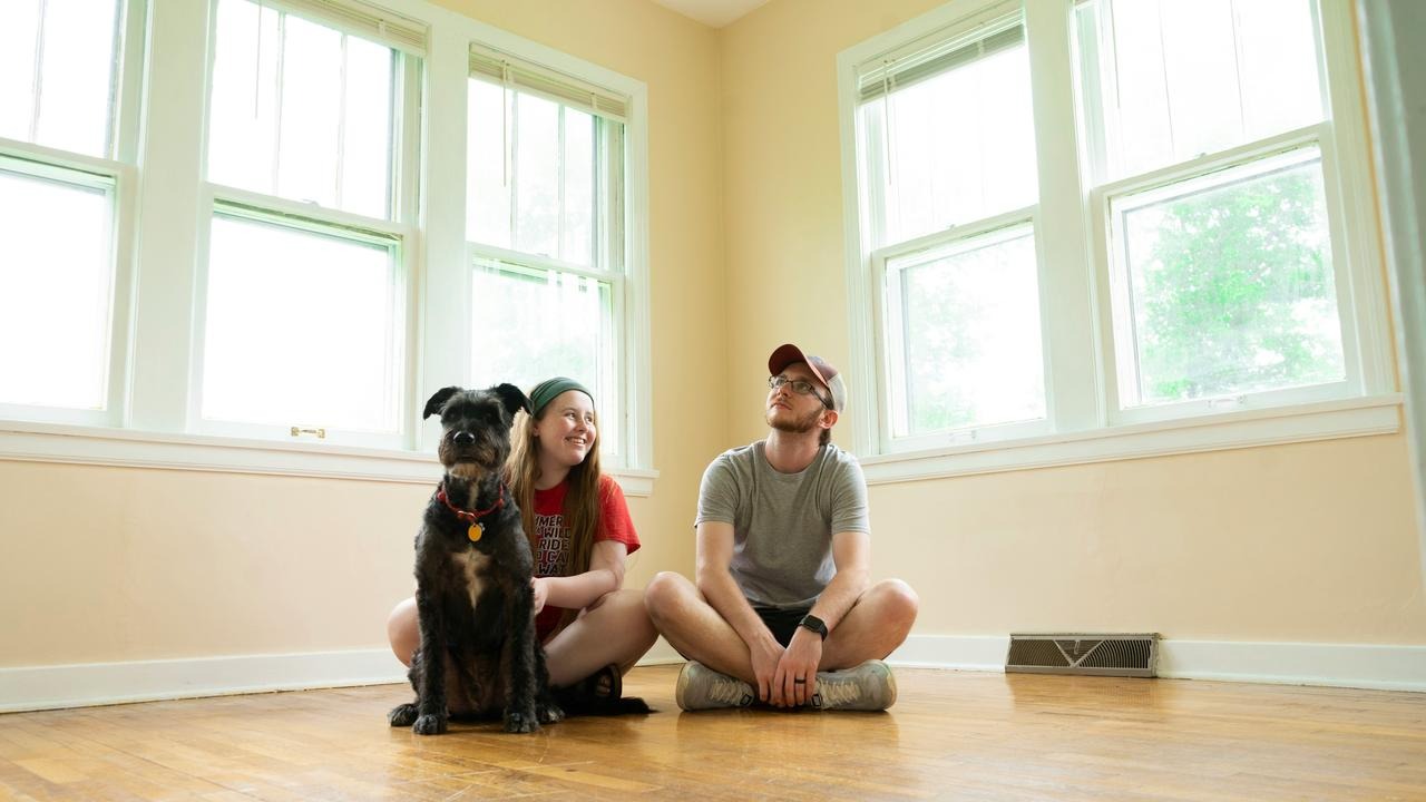 A couple sitting on the floor with their dog in a bright, empty room.