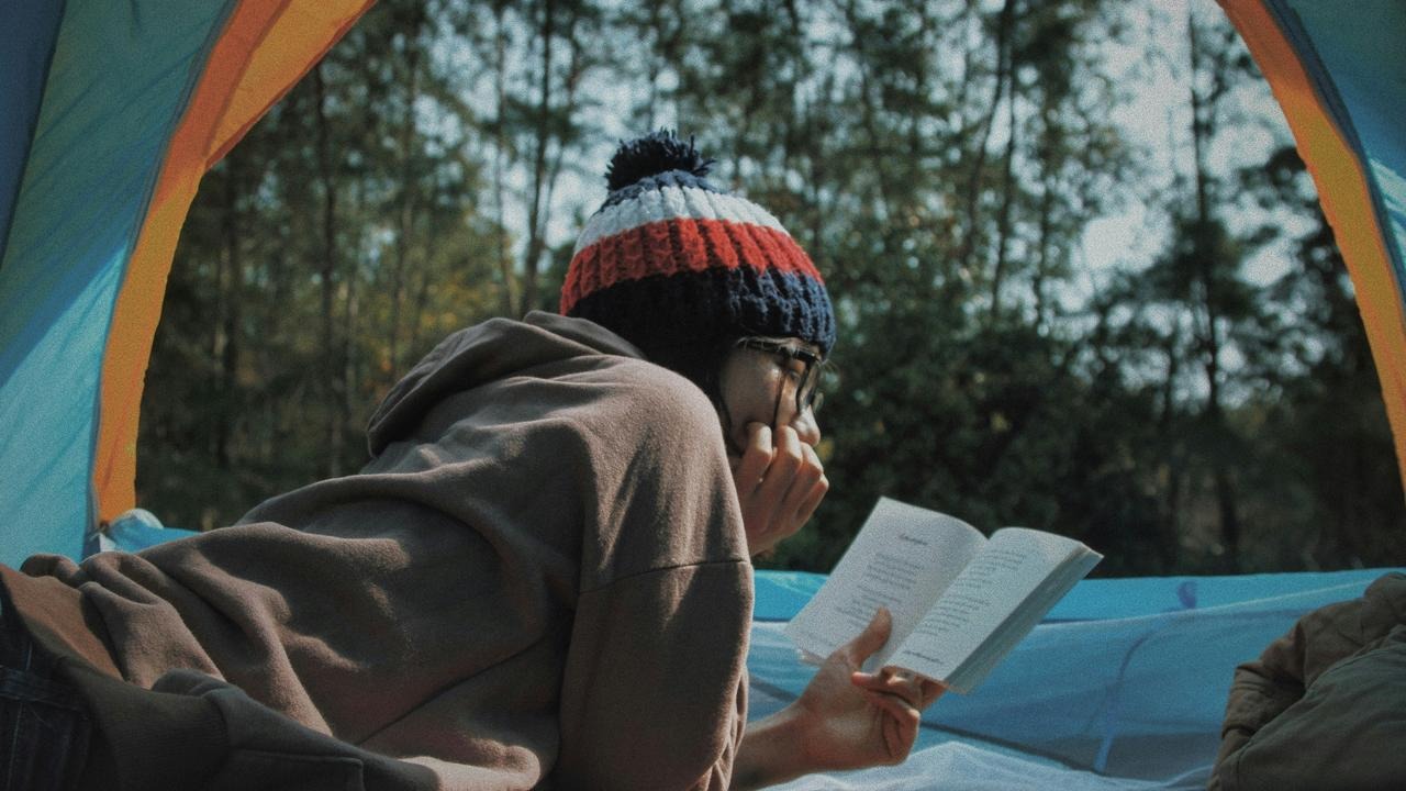 A person reading a book inside a tent in a forest.