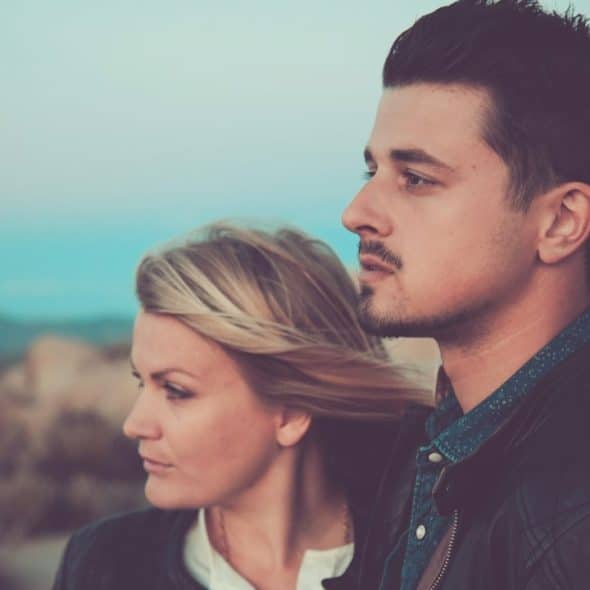 A couple standing on a beach and gazing into the distance together.