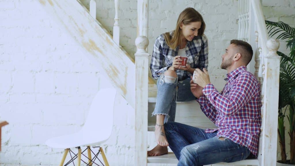 A couple talking to each other while having coffee and sitting on some stairs.