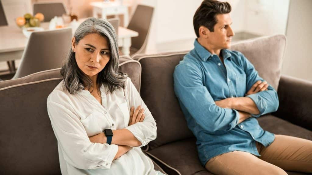 A man and woman sit on a sofa with arms crossed, looking away from each other.