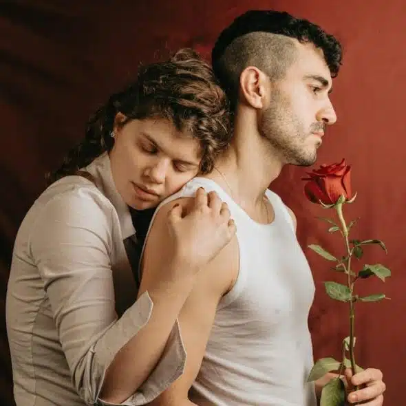 A woman hugging a man holding a rose from the backside.