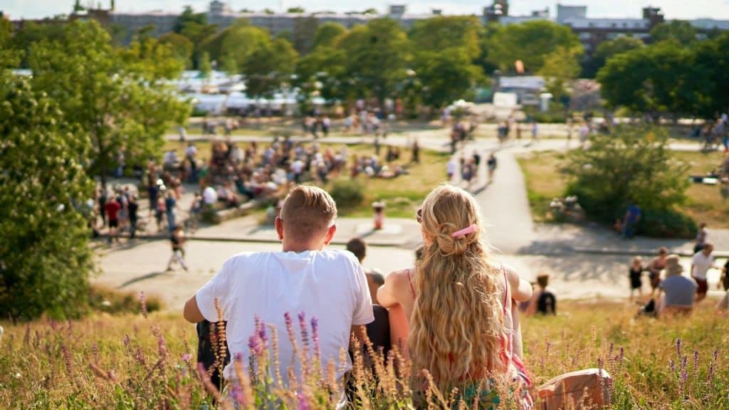 A couple sitting on a cliff overlooking a park and talking to each other.