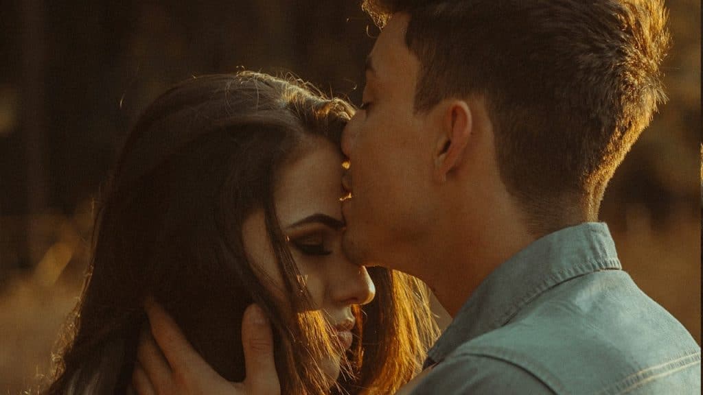 A man kissing a woman’s forehead while both of them have their eyes closed.