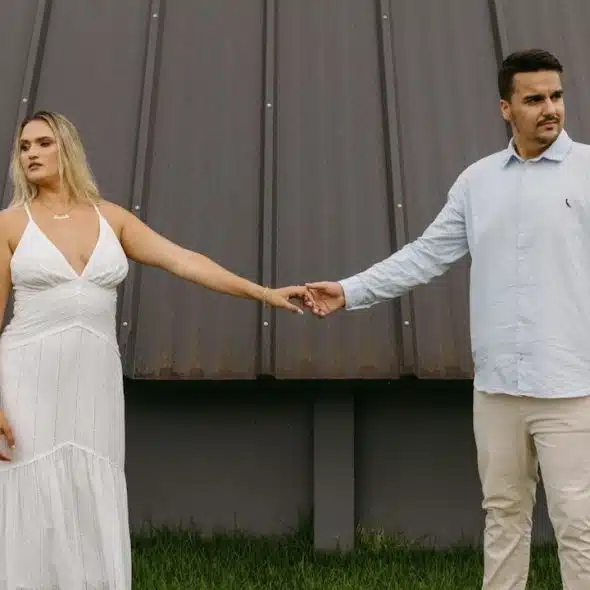 A couple standing apart from each other while holding hands and looking in opposite directions.