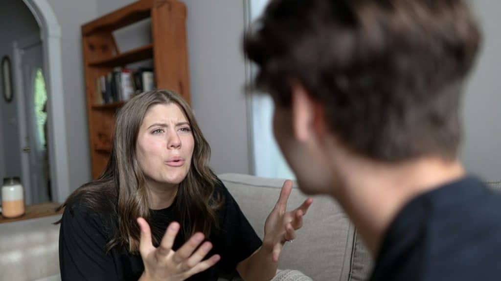 A woman gestures with her hands while speaking to a blurred man in a room.