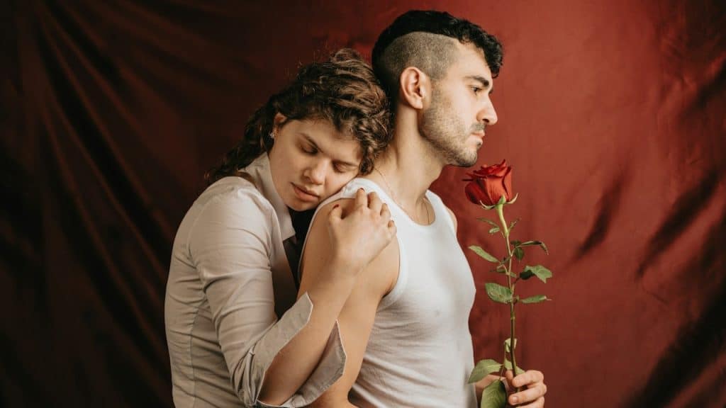 A woman hugging a man holding a rose from the backside.