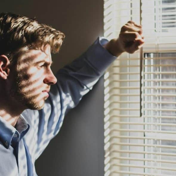 A man standing by a window with blinds.