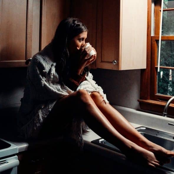 A woman sitting on a kitchn counter and drinking coffee.