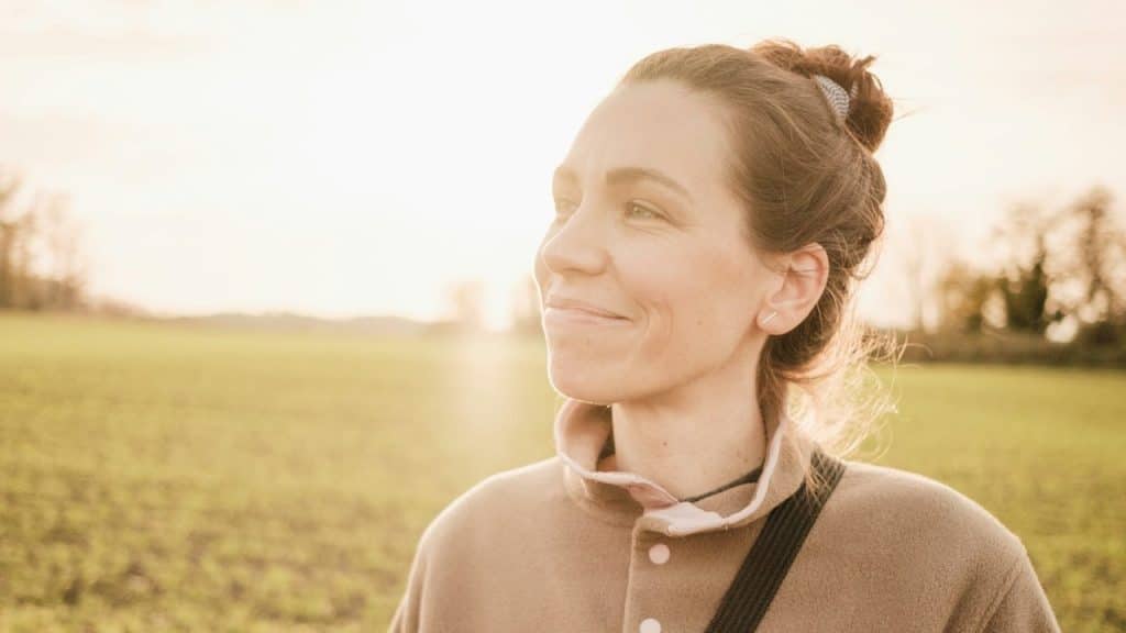 A woman with her hair tied back is standing in a field.