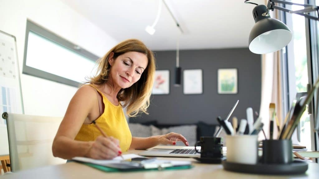 A woman writing something on a paper while performing calculations on a calculator.