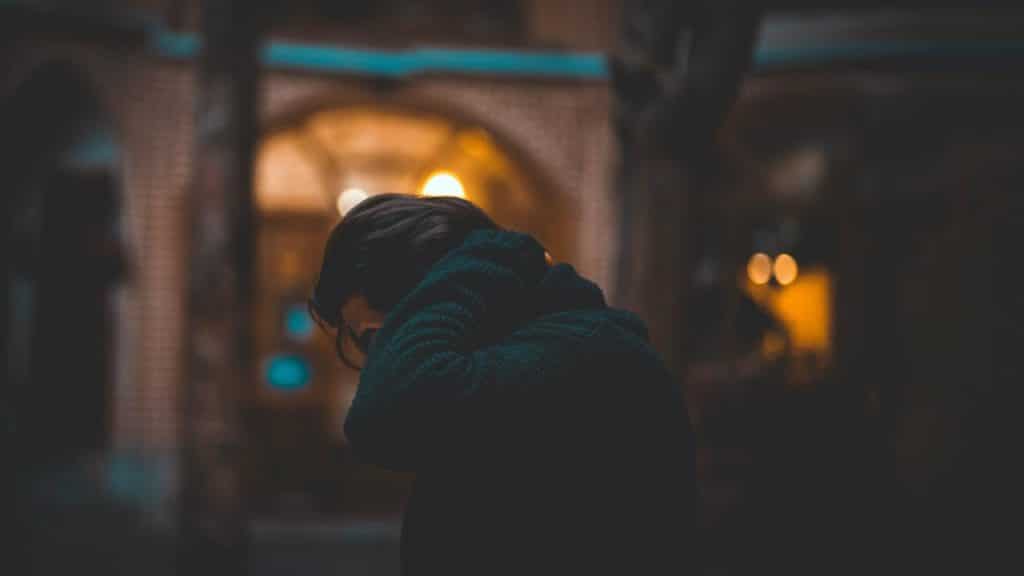 A person in a dark coat looking down under warm city lights.