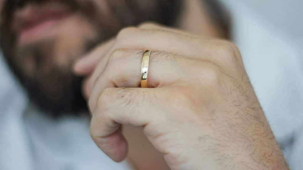 A close-up of a man's hand touching his chin, highlighting a gold band ring.