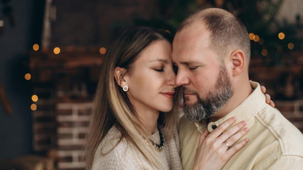 A couple embracing with eyes closed in a warmly lit indoor setting.