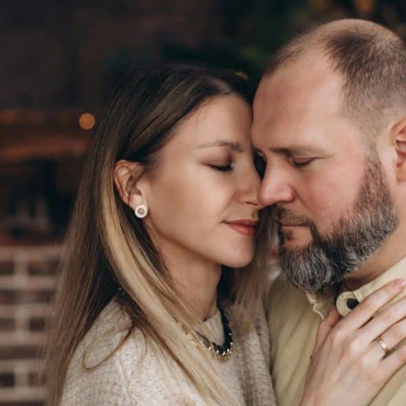 A couple embracing with eyes closed in a warmly lit indoor setting.