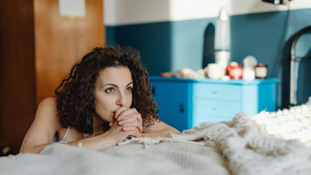 A woman lying on a bed, looking thoughtful.