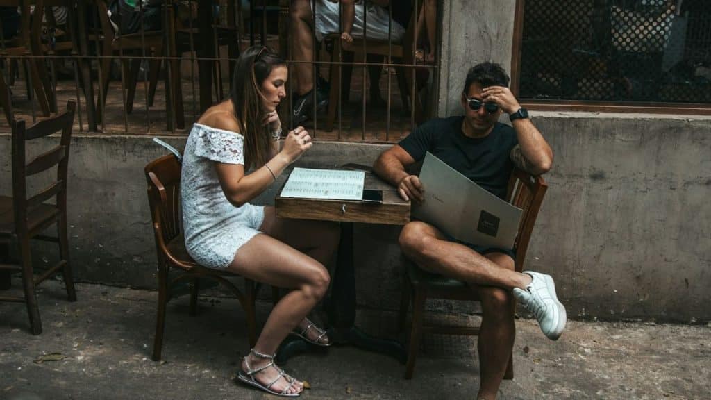A woman in a white lace dress and a man in a black shirt read menus.