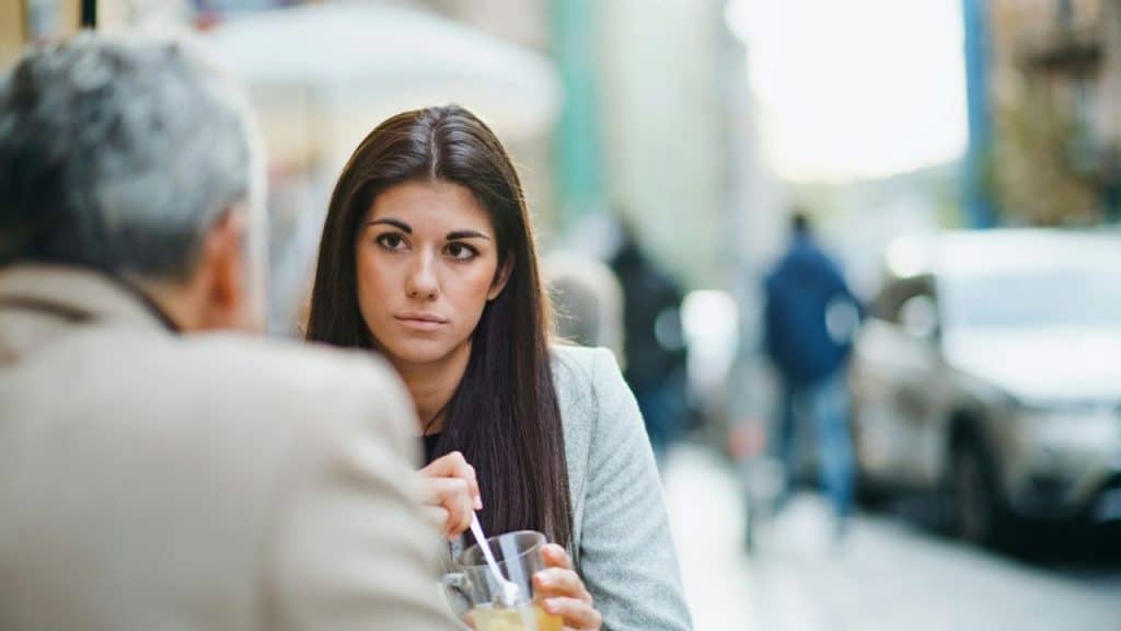 A woman with long dark hair looks toward a person whose back is to the camera.