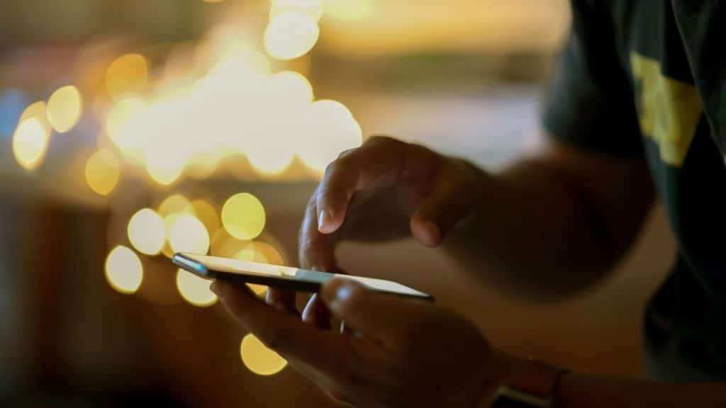 Close-up of hands using a smartphone with golden bokeh lights blurred in the background.