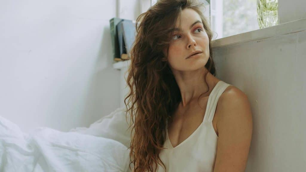 A woman sitting by a window, gazing away.