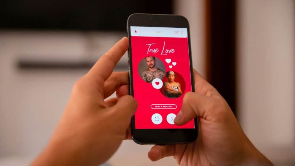 Hands hold a smartphone displaying a red mobile app interface with two circular profile photos.