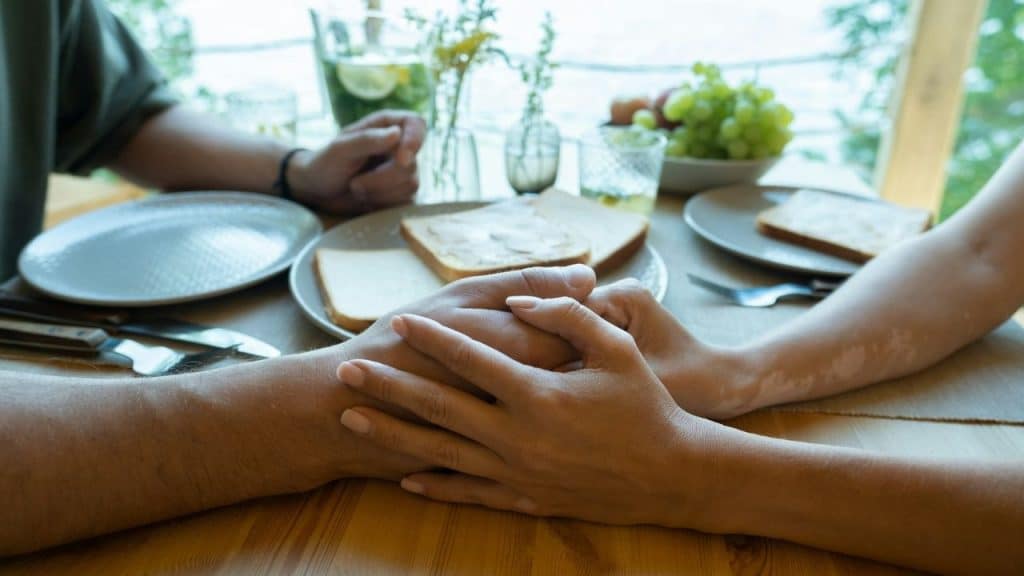 Close-up of two people holding hands over a table set with toast and green grapes.