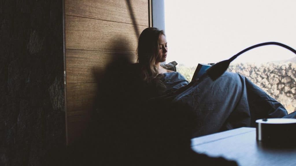 A woman reading in bed by a window.