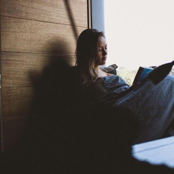 A woman reading in bed by a window.