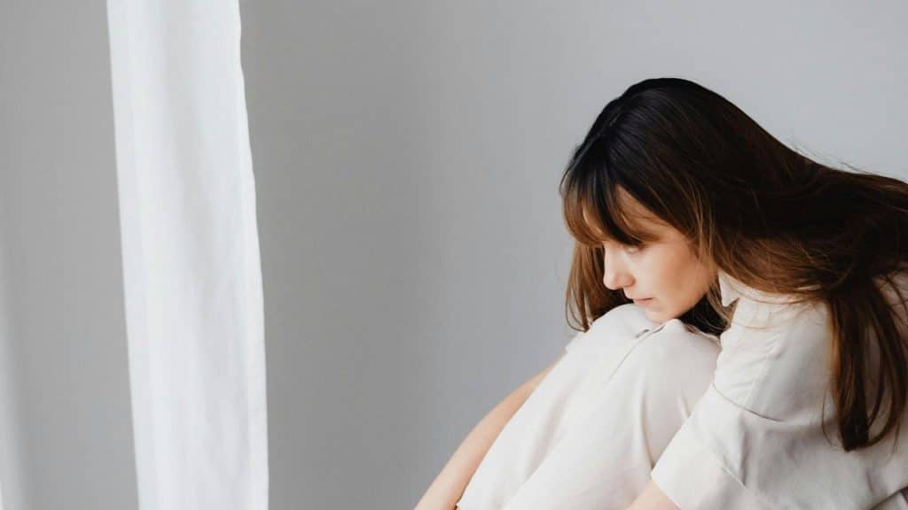 A woman sitting curled up, looking down thoughtfully.