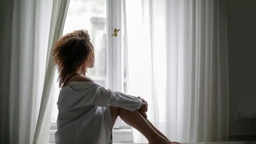 A woman sitting by a window, looking outside.