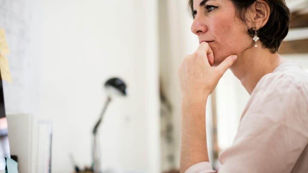 A woman sitting at a desk with her hand on her chin looking thoughtful.