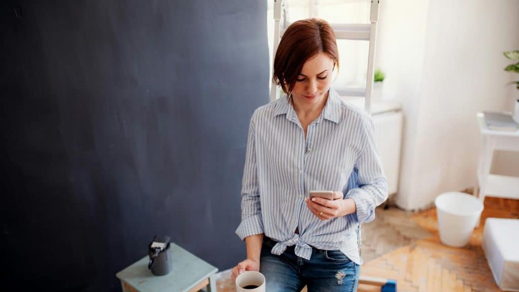 A woman holding a coffee cup while looking at her phone.