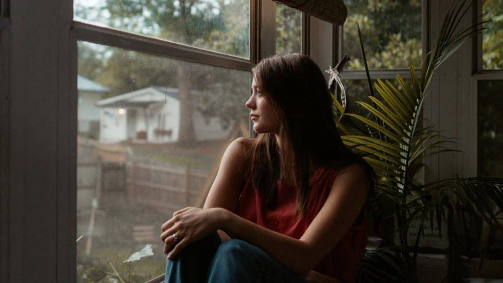 A woman sitting by a window looking outside thoughtfully.