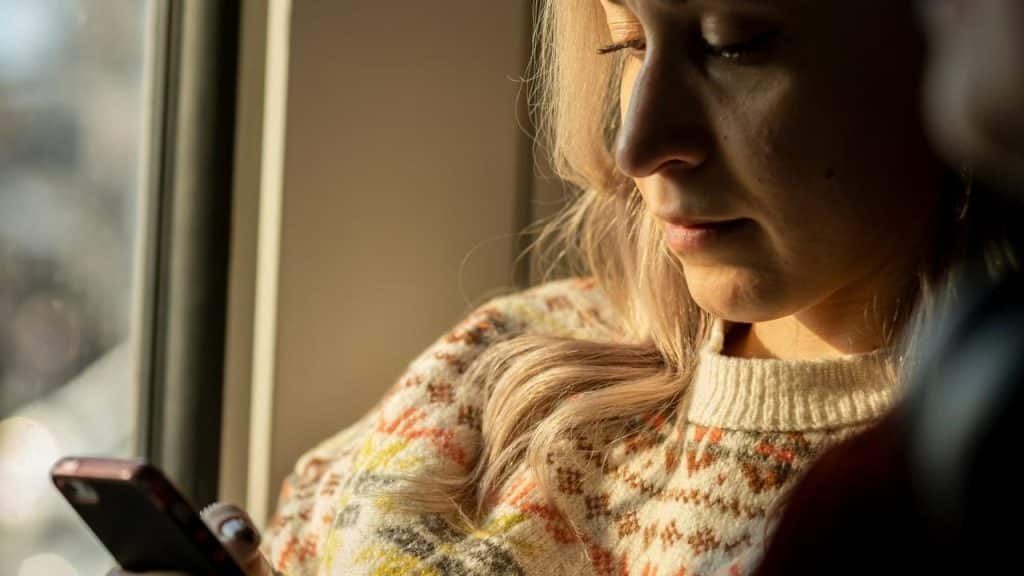 A woman looking at her phone while sitting by a window.