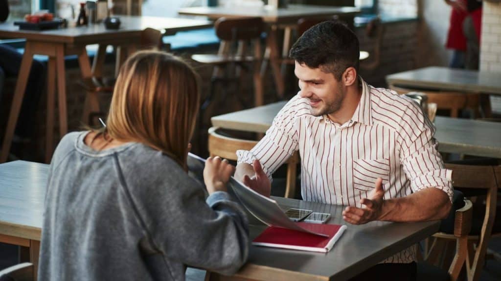 Two people sit at a table in a restaurant while looking at a paper menu.