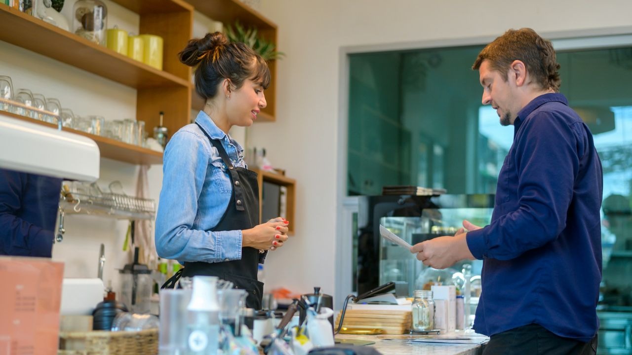 A man stands at a cafe counter holding a small slip of paper near a server.