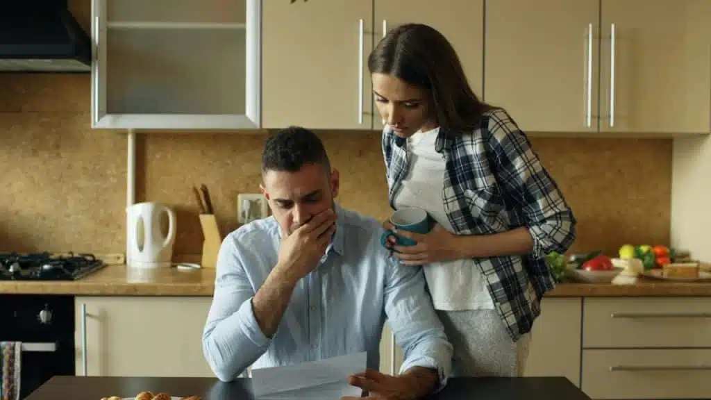 A man and woman in a kitchen look down at a piece of paper held by the man.