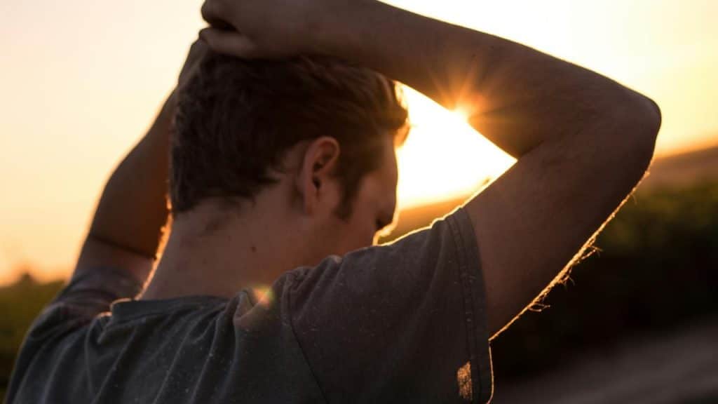 A person seen from behind with hands in their hair, standing outdoors at sunset.