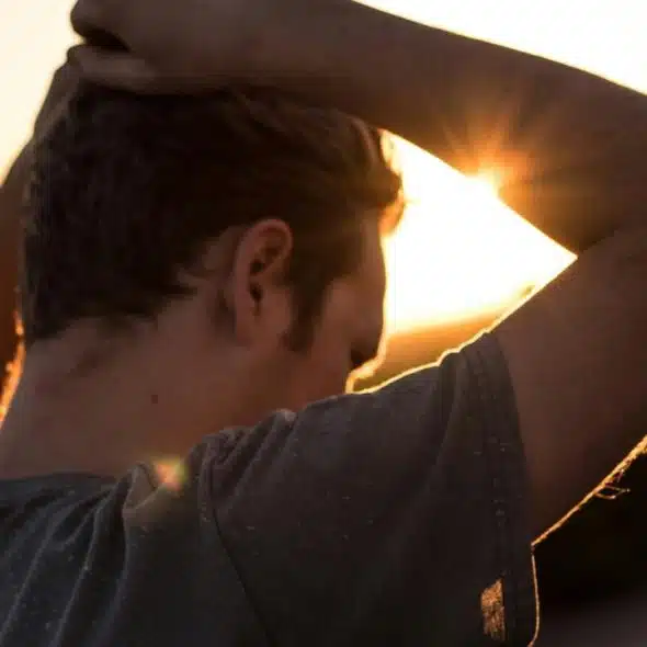 A person seen from behind with hands in their hair, standing outdoors at sunset.