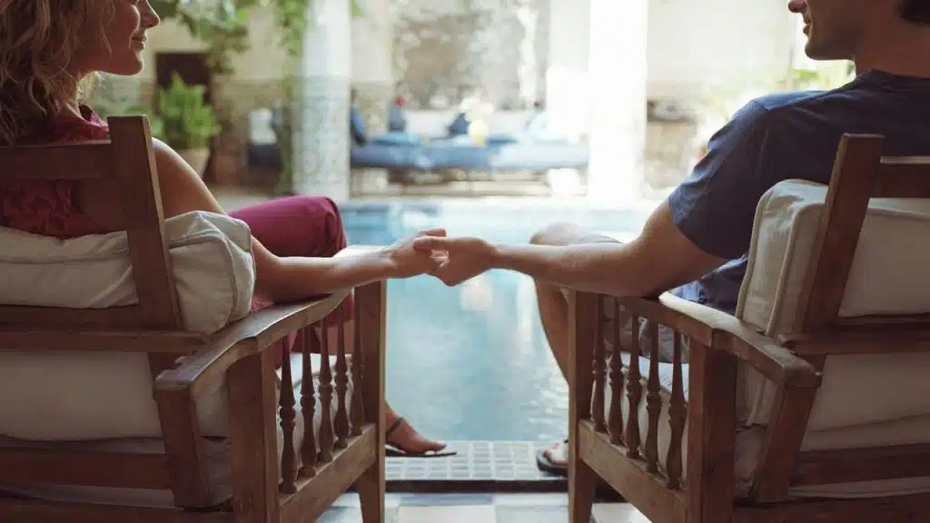 A couple holding hands while sitting by a pool.