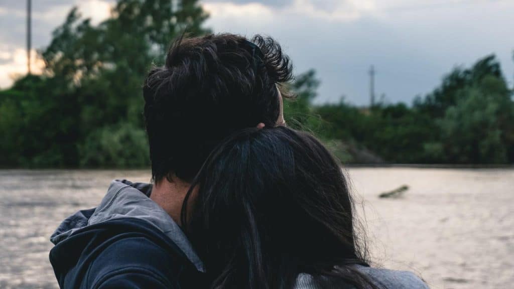 A couple sitting by the water with their heads close together.