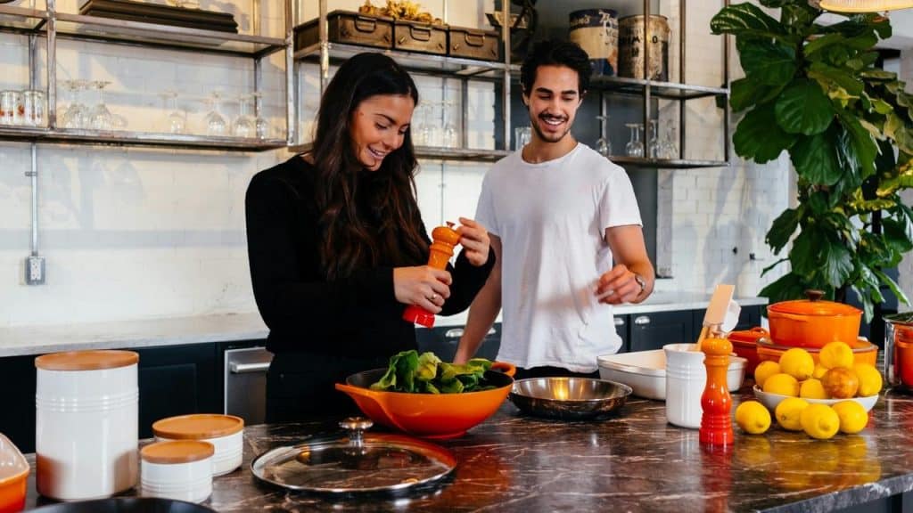 A smiling couple preparing food together in a modern kitchen.