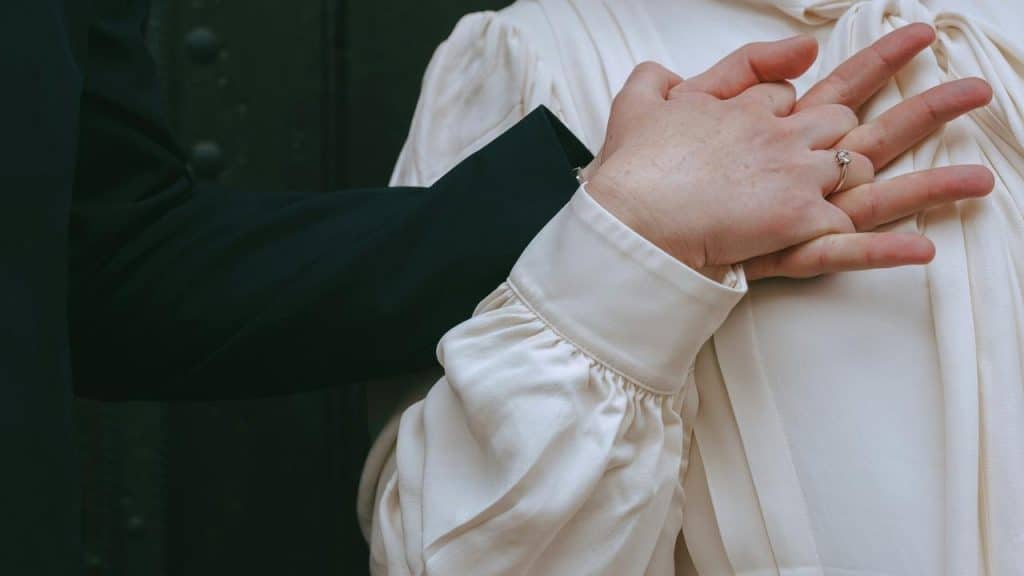 A close-up of two people holding hands, one wearing an engagement ring.