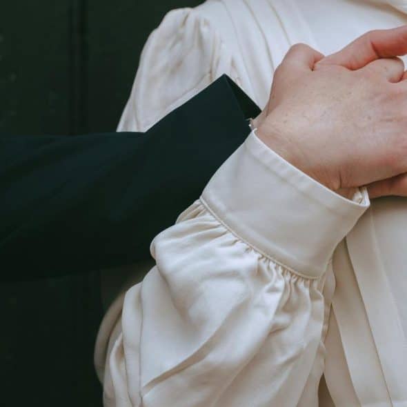 A close-up of two people holding hands, one wearing an engagement ring.