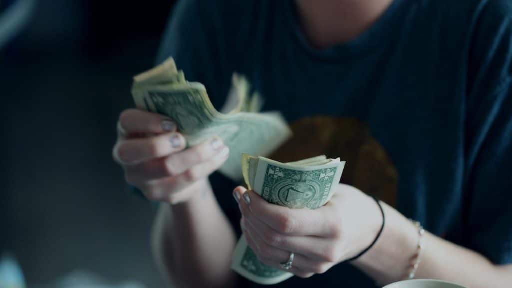 A person counting a stack of U.S. dollar bills.