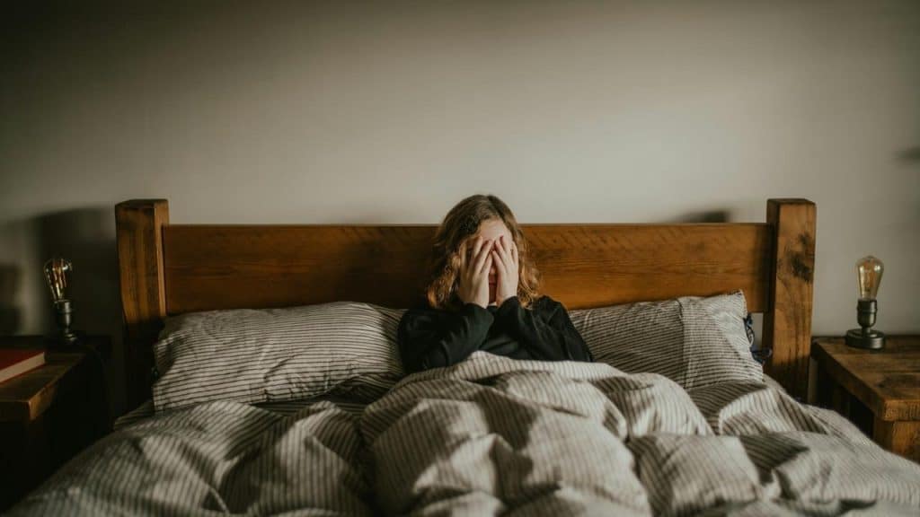 A person sitting up in bed with hands covering their face.
