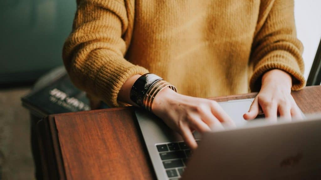 A person typing on a laptop at a wooden desk.
