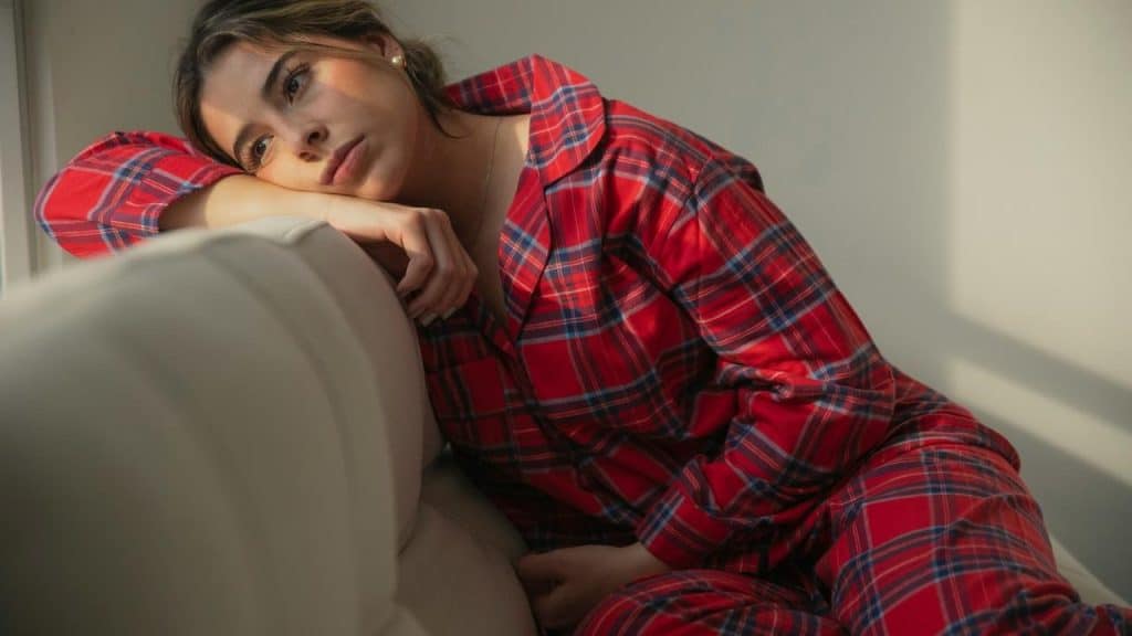 A woman in red plaid pajamas resting her head on a couch.